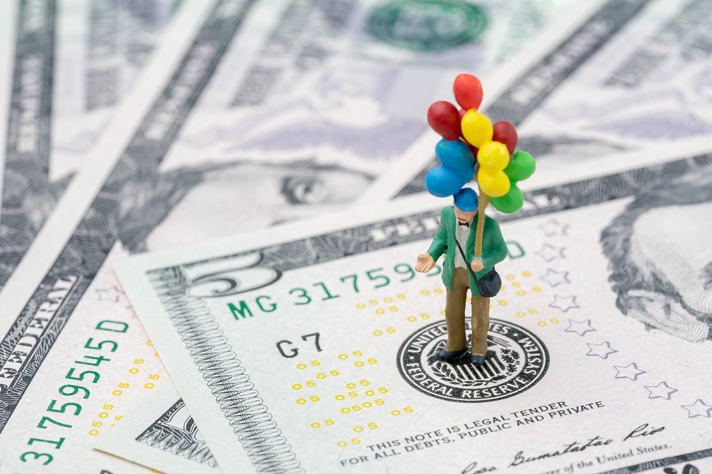 Plastic figure with a bunch of colourful balloons stood on a dollar bill